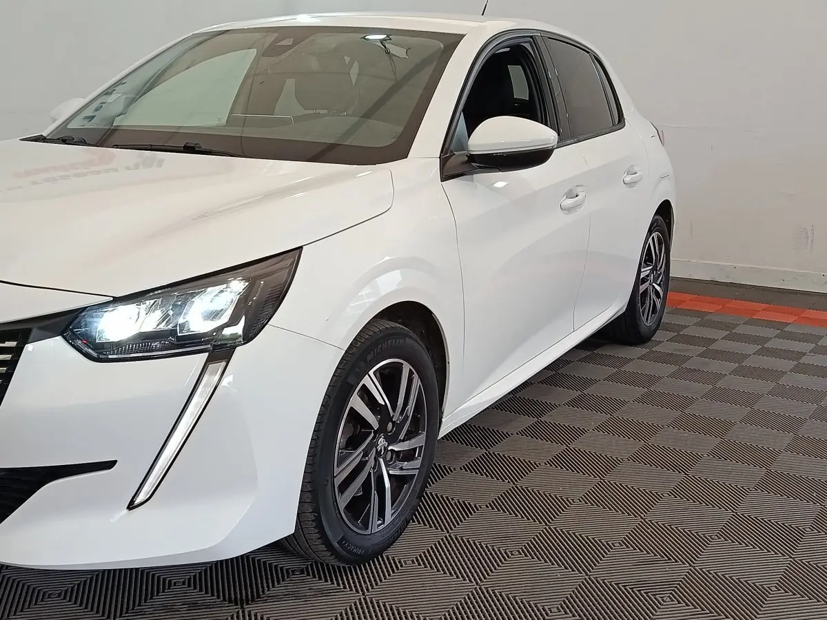 Peugeot 208 blanc vue 3/4 avant droit avec phares LED allumés et jantes alliage noires.