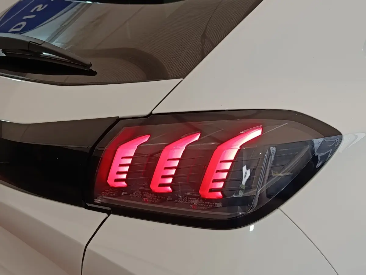 Gros plan sur le feu arrière droit allumé d'une Peugeot 208 blanche, soulignant son design à trois griffes LED.