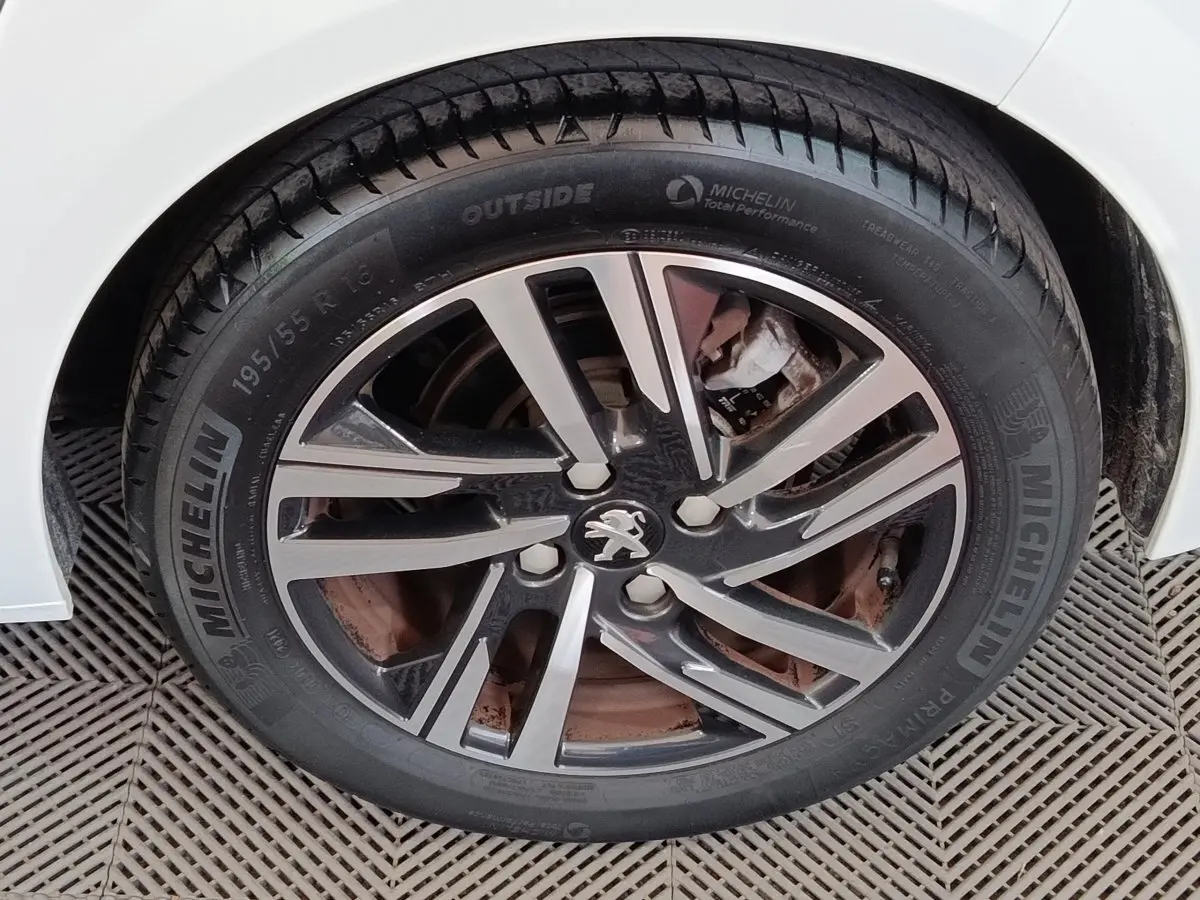 Gros plan sur la roue avant droite d'une Peugeot 208 blanche, avec jante alliage et pneu Michelin visible.