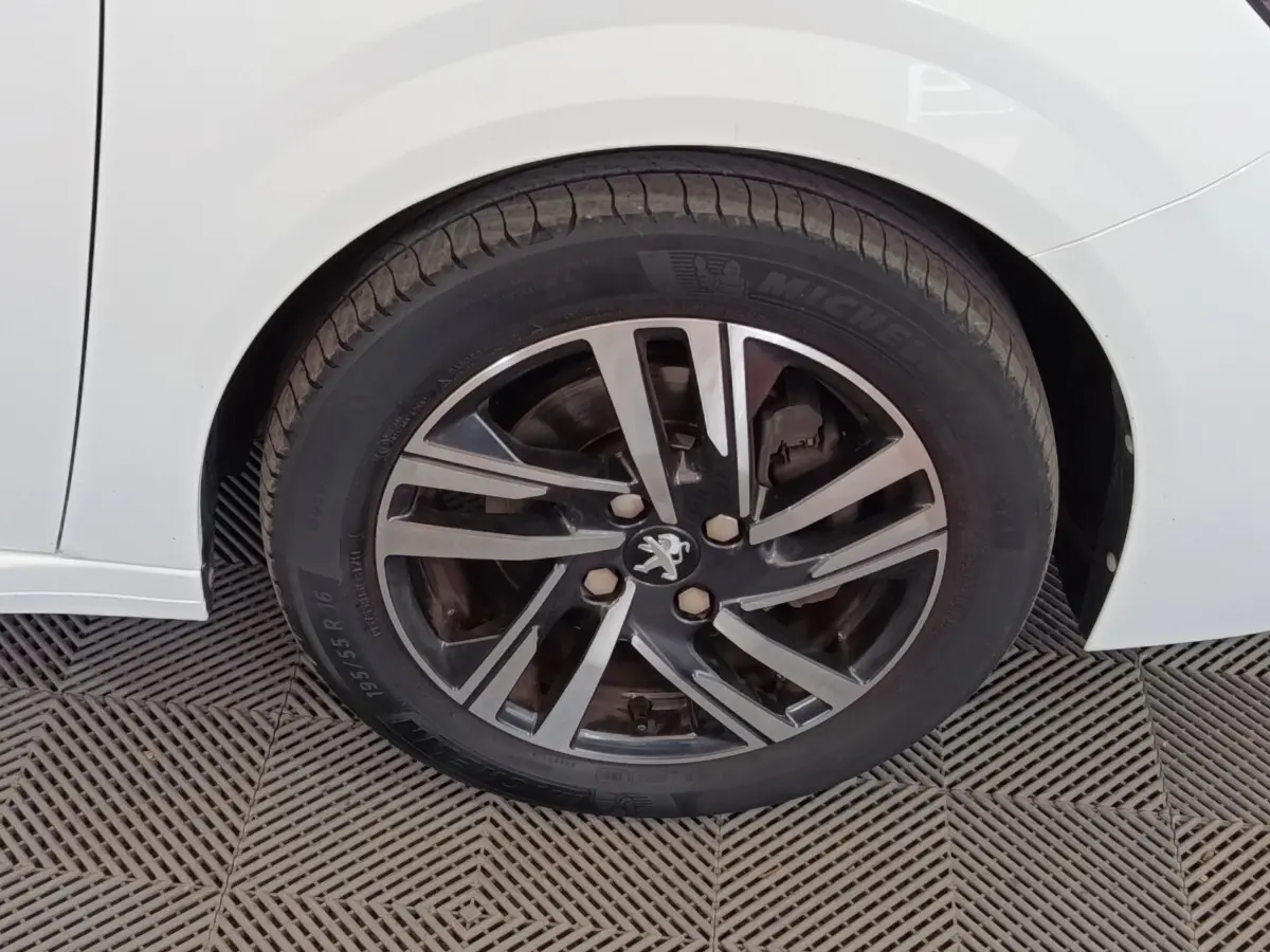 Gros plan sur la roue avant droite d'une Peugeot 208 blanche, avec jante alliage noire et argentée au design moderne.
