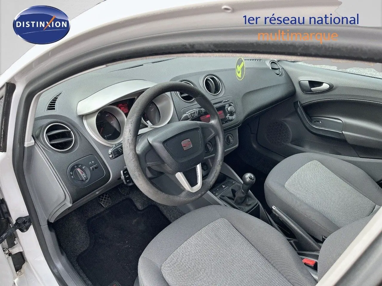 Intérieur de la SEAT Ibiza 1.6 TDI 90CH STYLE 2010 blanche, vue côté conducteur montrant volant, tableau de bord et sièges gris.