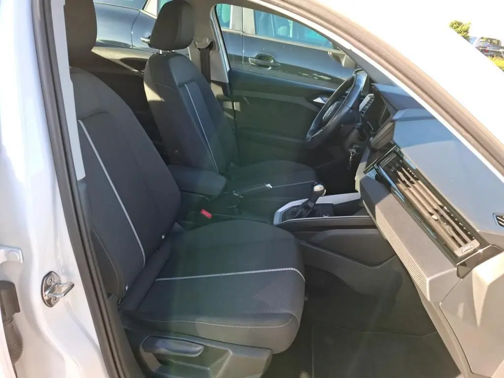 Vue rapprochée de la porte arrière gauche noire ouverte d’un Audi A1 blanc, avec poignée intérieure argentée.