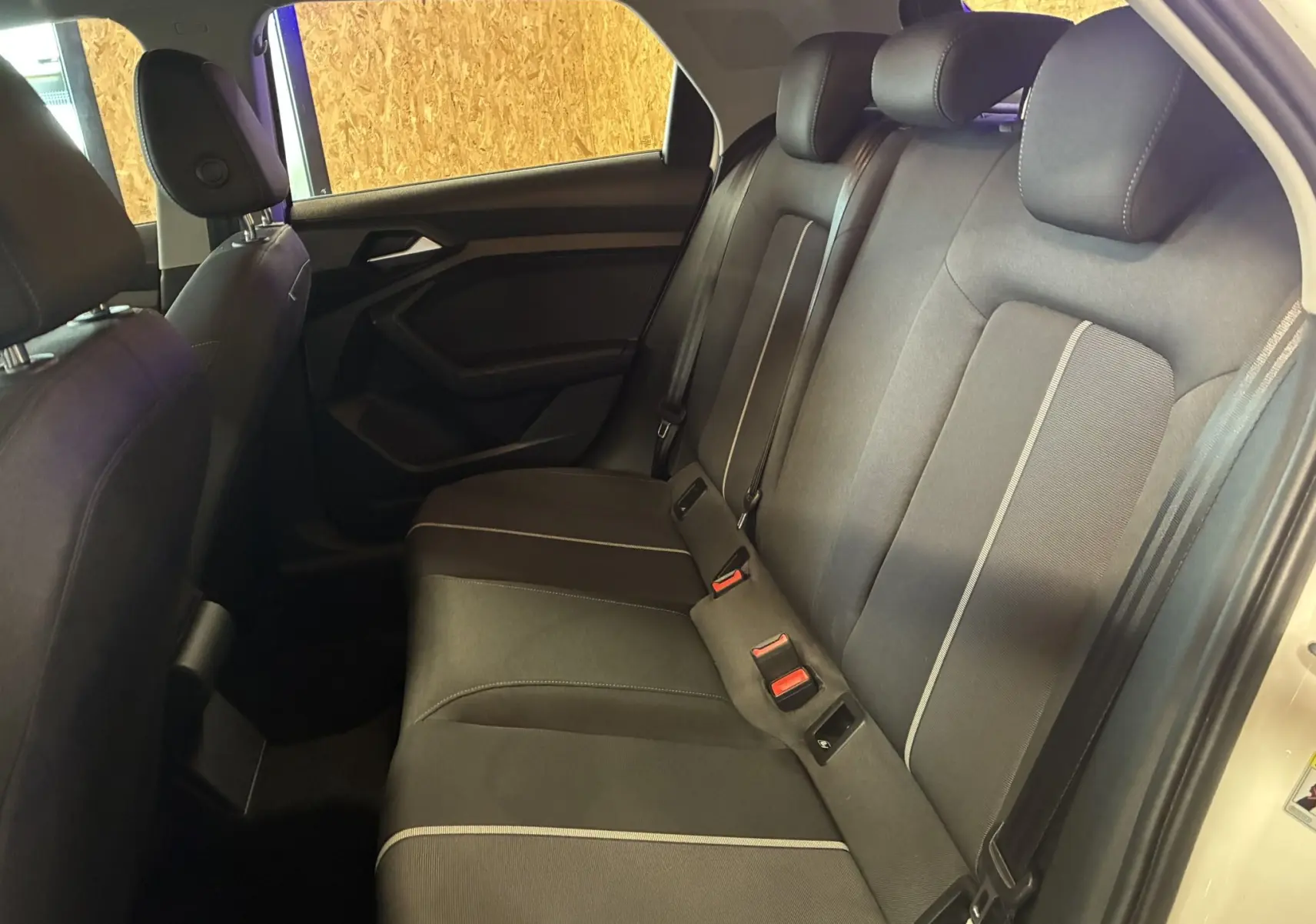 Vue intérieure côté droit sur la banquette arrière tissu gris foncé de l'Audi A1 blanche, avec ceintures et appuie-têtes visibles.