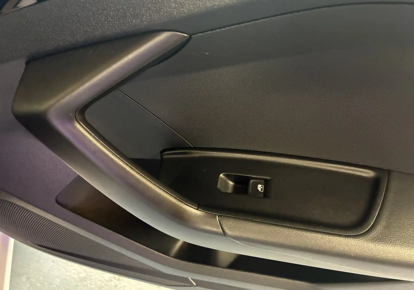 Gros plan sur la poignée intérieure noire de la porte côté gauche d'une Audi A1 blanche, avec bouton de commande de vitre.