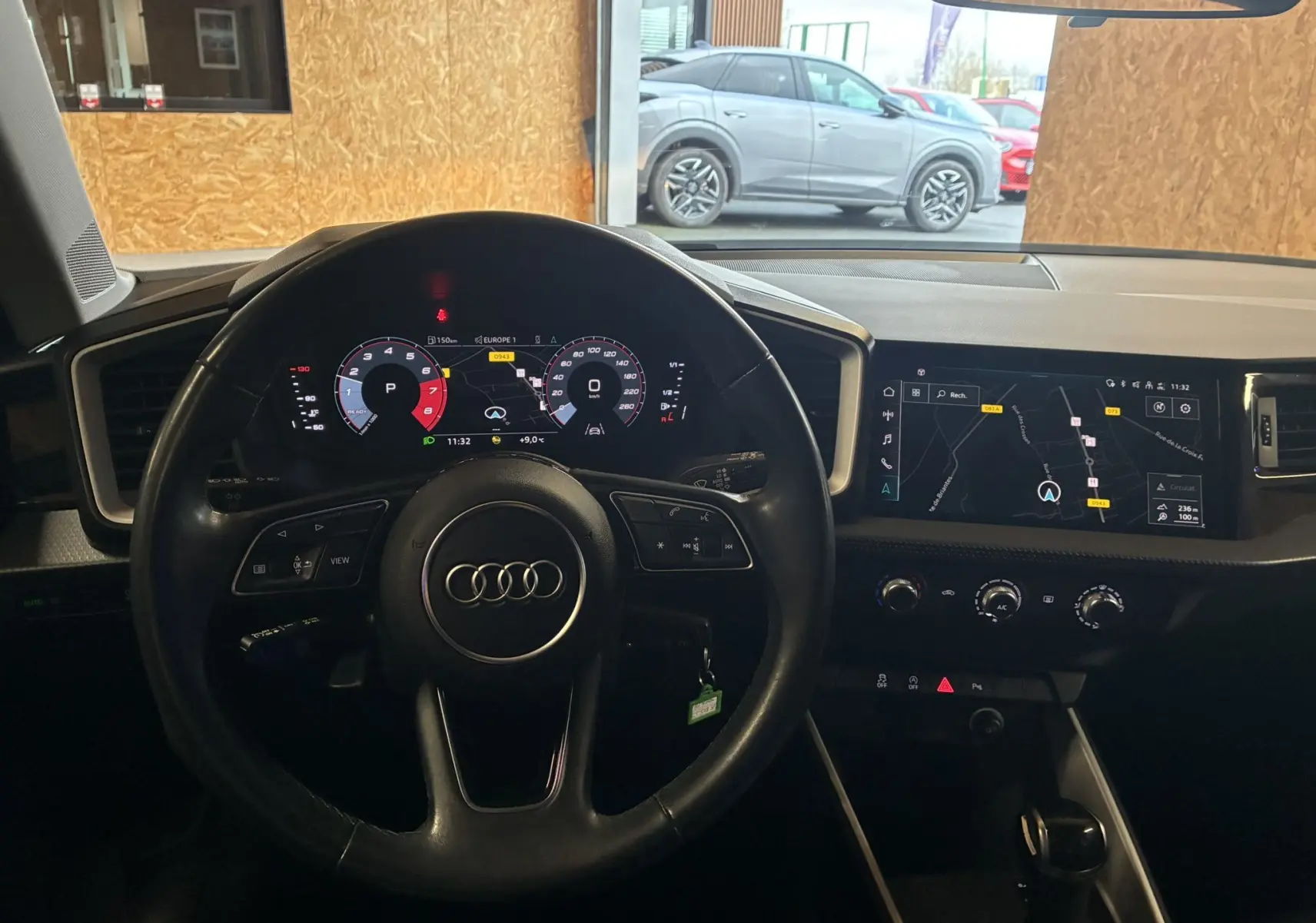 Vue intérieure centrée sur le volant cuir et le cockpit numérique de l'Audi A1, avec écran GPS et tableau de bord noir.