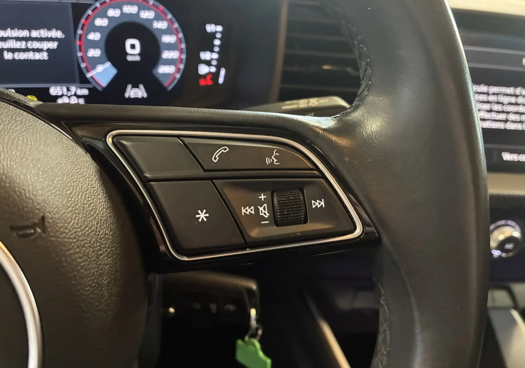 Gros plan sur les commandes multifonctions du volant cuir noir d'une Audi A1 2022, avec tableau de bord numérique en arrière-plan.