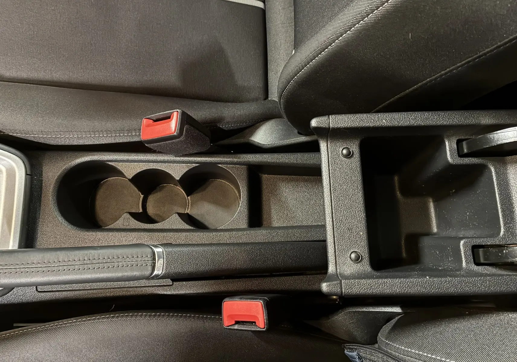 Vue rapprochée de la console centrale noire avec porte-gobelets et frein à main sur Audi A1 blanche 2022.