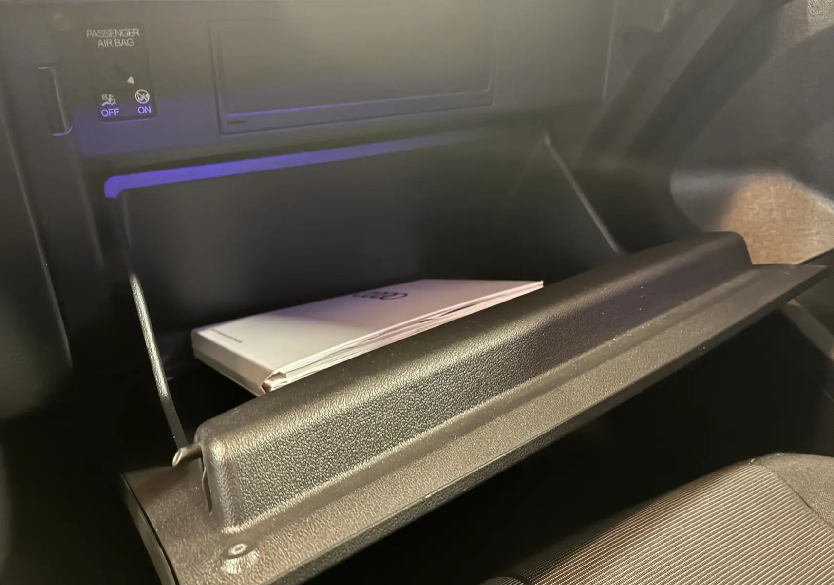 Gros plan sur la boîte à gants ouverte de l'Audi A1 2022 avec manuel blanc visible à l'intérieur.
