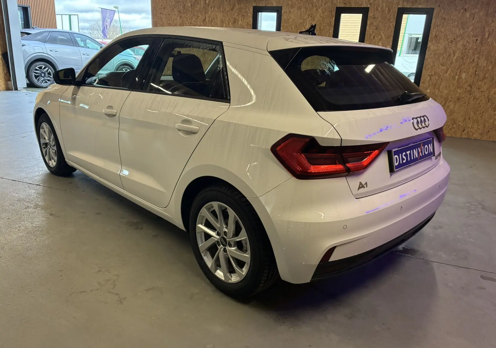 Vue 3/4 arrière droite d'une Audi A1 blanche avec jantes alu 17 pouces, garée en intérieur sur sol béton.