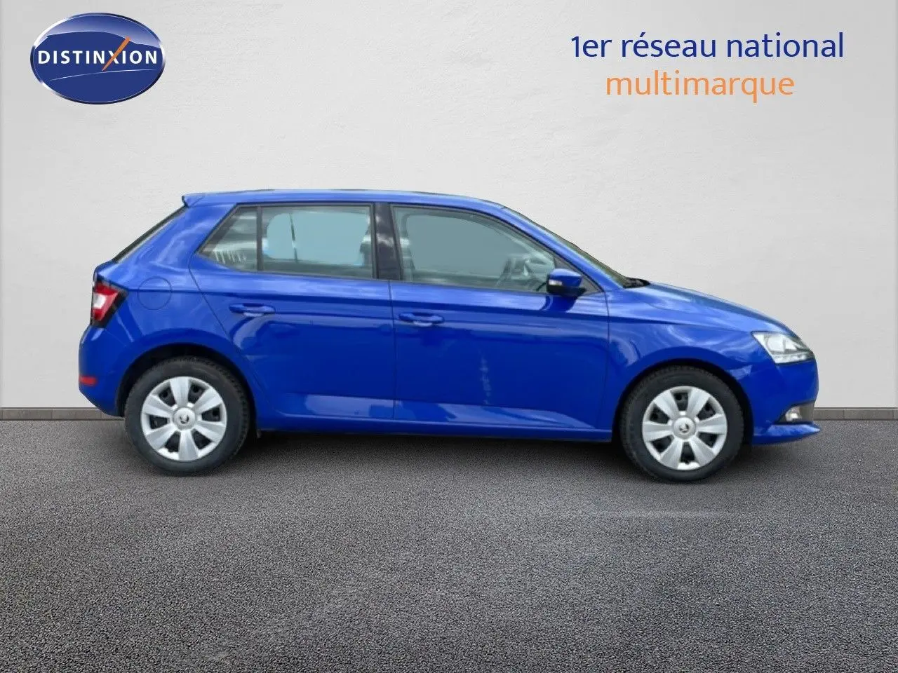 Vue 3/4 arrière droite d'une Skoda Fabia 2019 bleu énergie garée en ville, avec feux arrière allumés.
