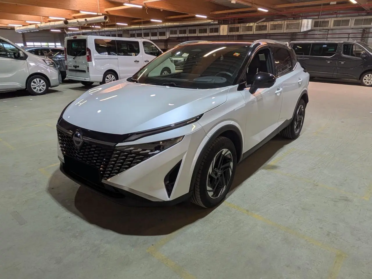 Nissan Qashqai blanc nacré avec toit noir, vu en 3/4 avant droit dans un parking intérieur.