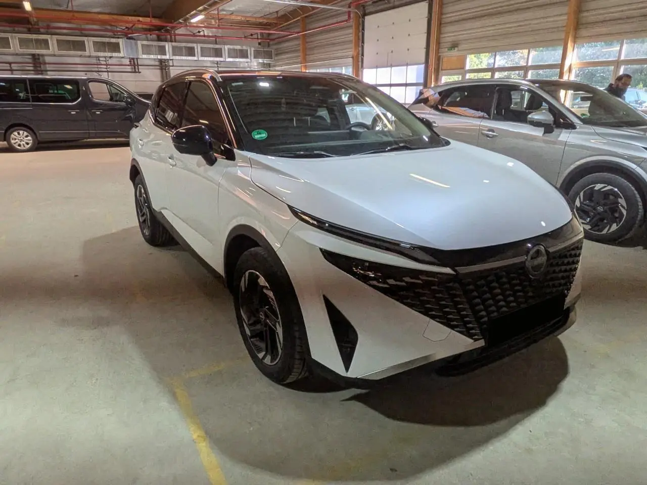 Nissan Qashqai blanc nacré avec toit noir, vu en 3/4 avant droit dans un garage intérieur.