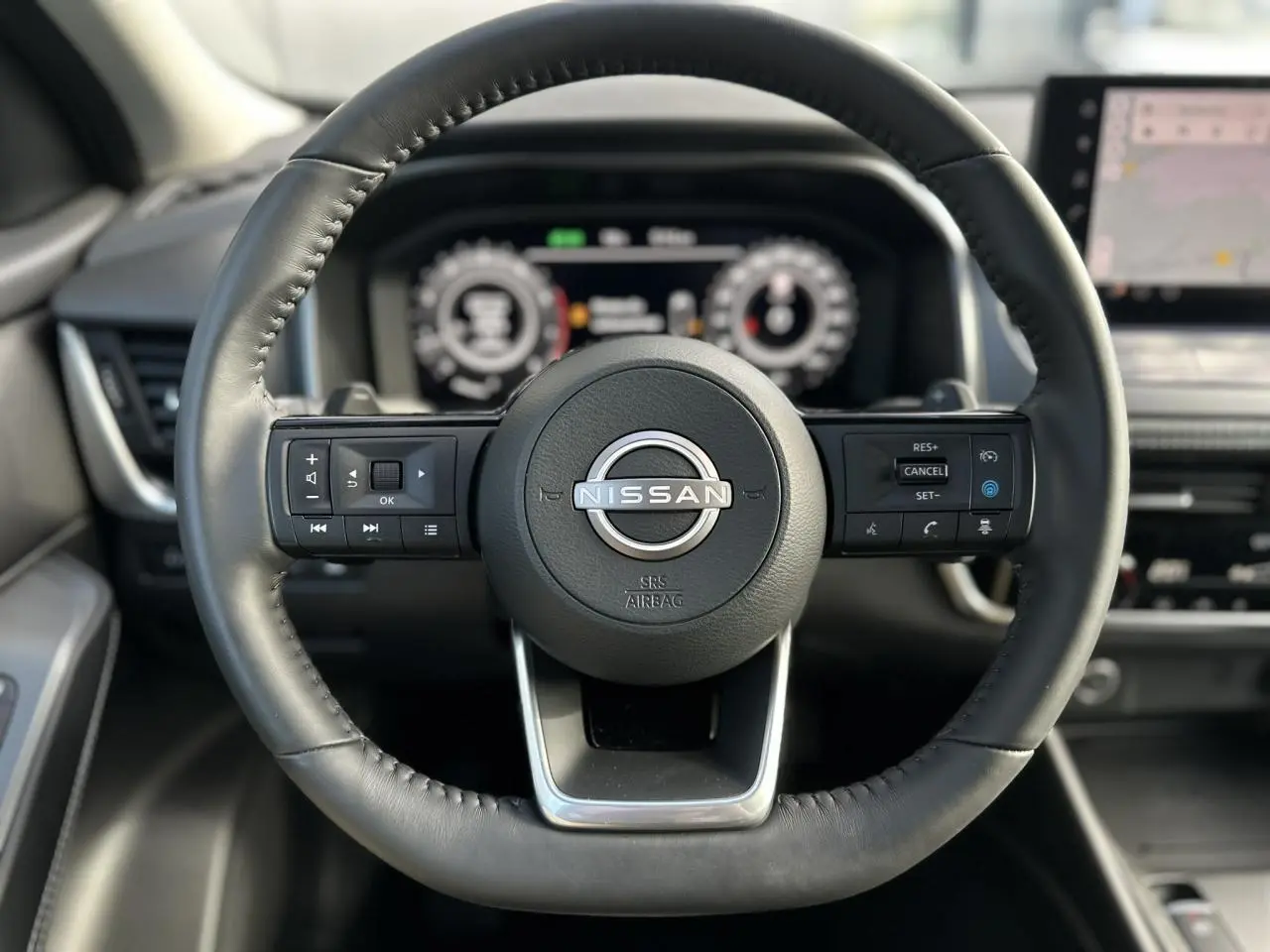 Volant cuir noir de Nissan Qashqai 2025 vu de face, avec commandes intégrées et tableau de bord numérique flou.