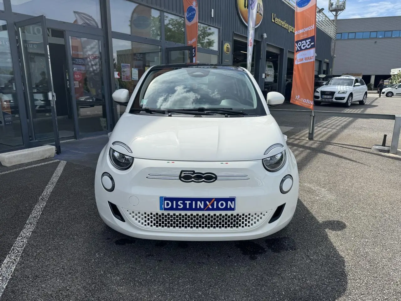 Vue frontale d'une Fiat 500 électrique blanche 2022 avec toit panoramique, stationnée devant un garage.