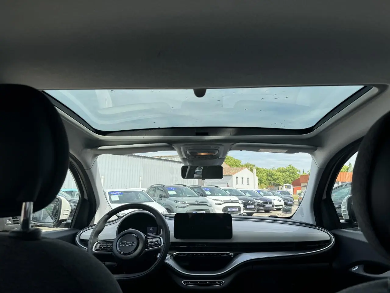 Vue intérieure avant de la Fiat 500 électrique blanche 2022, mettant en valeur le toit vitré panoramique et le tableau de bord épuré.