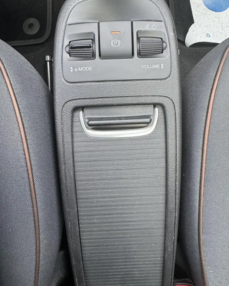 Vue rapprochée de la console centrale noire entre les sièges gris anthracite de la Fiat 500 électrique blanche.