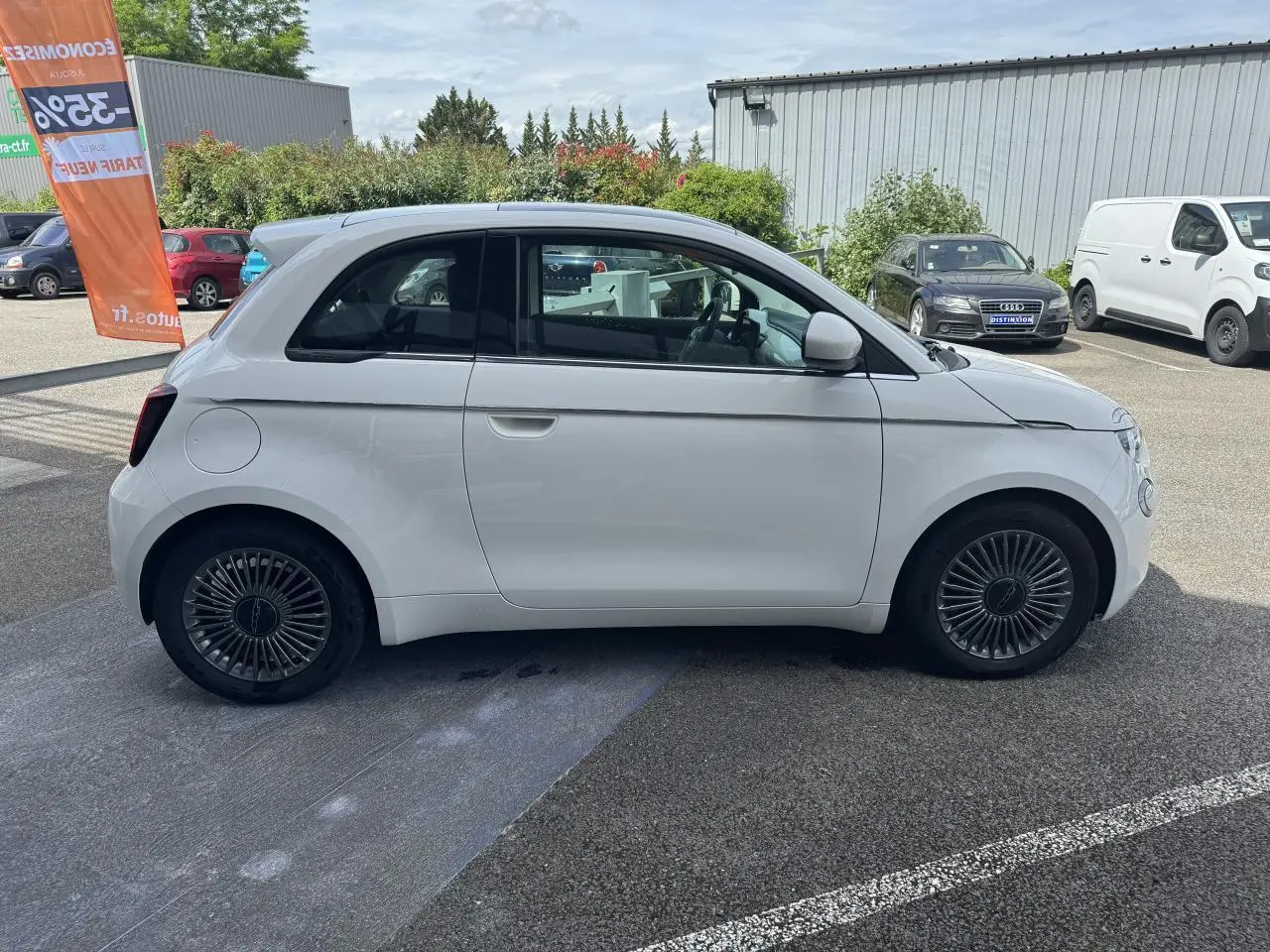 Profil droit d'une Fiat 500 électrique blanche 2022 avec jantes alliage 16'' Icône sur parking extérieur.