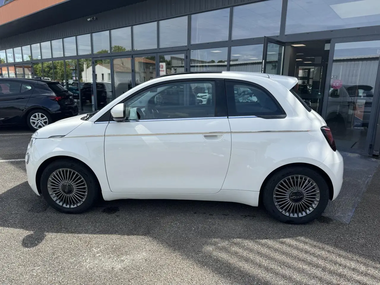 Profil côté gauche d'une Fiat 500 électrique blanche 2022 avec jantes alliage 16'' et toit panoramique visible.
