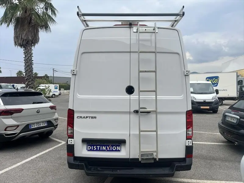 Vue arrière d'un Volkswagen Crafter blanc L3H3 avec échelle et galerie sur le toit, stationné en extérieur.