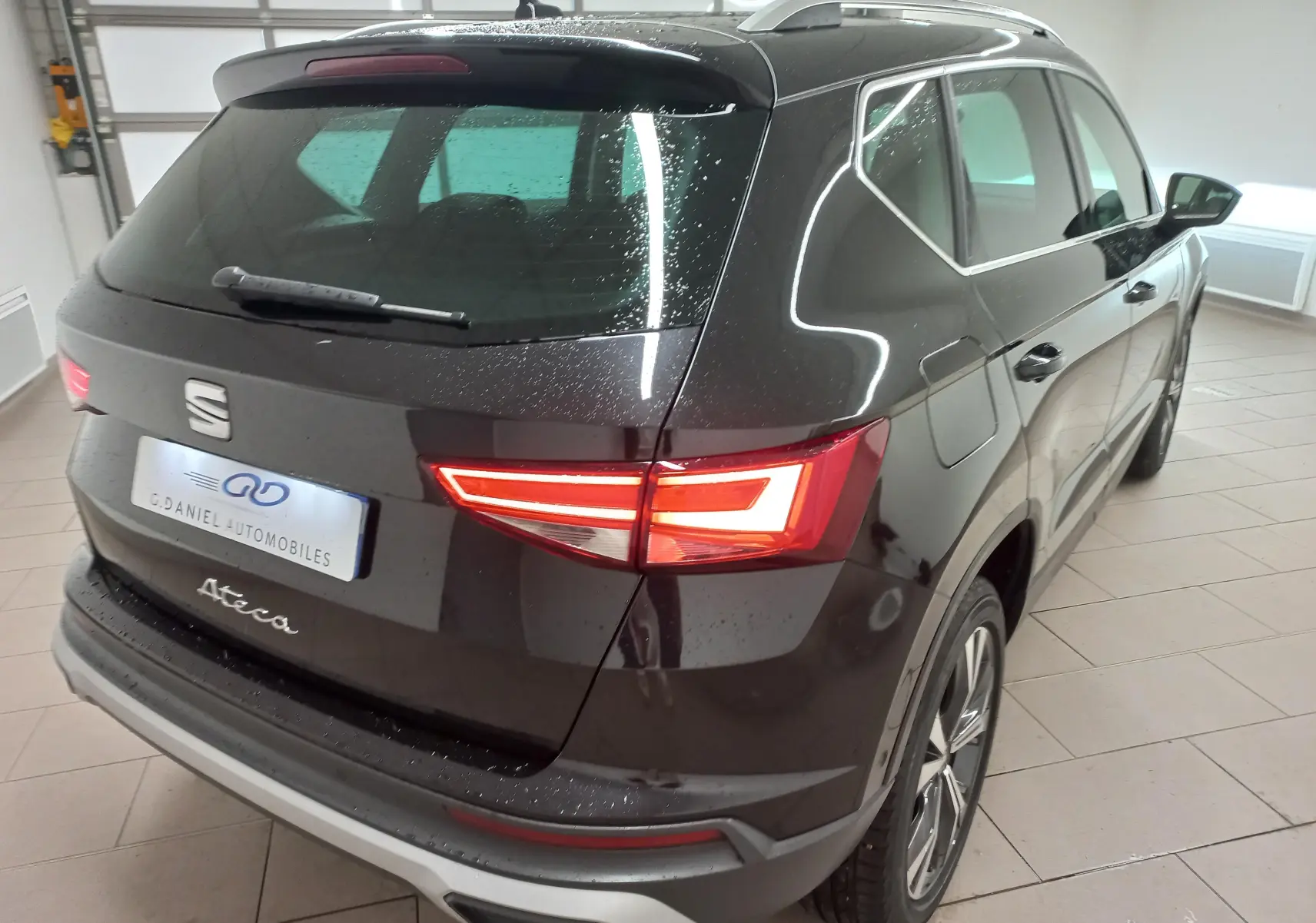 Vue 3/4 arrière droite du SEAT Ateca noir Magic Nacré avec feux allumés et jantes alliage 18 pouces en intérieur showroom.