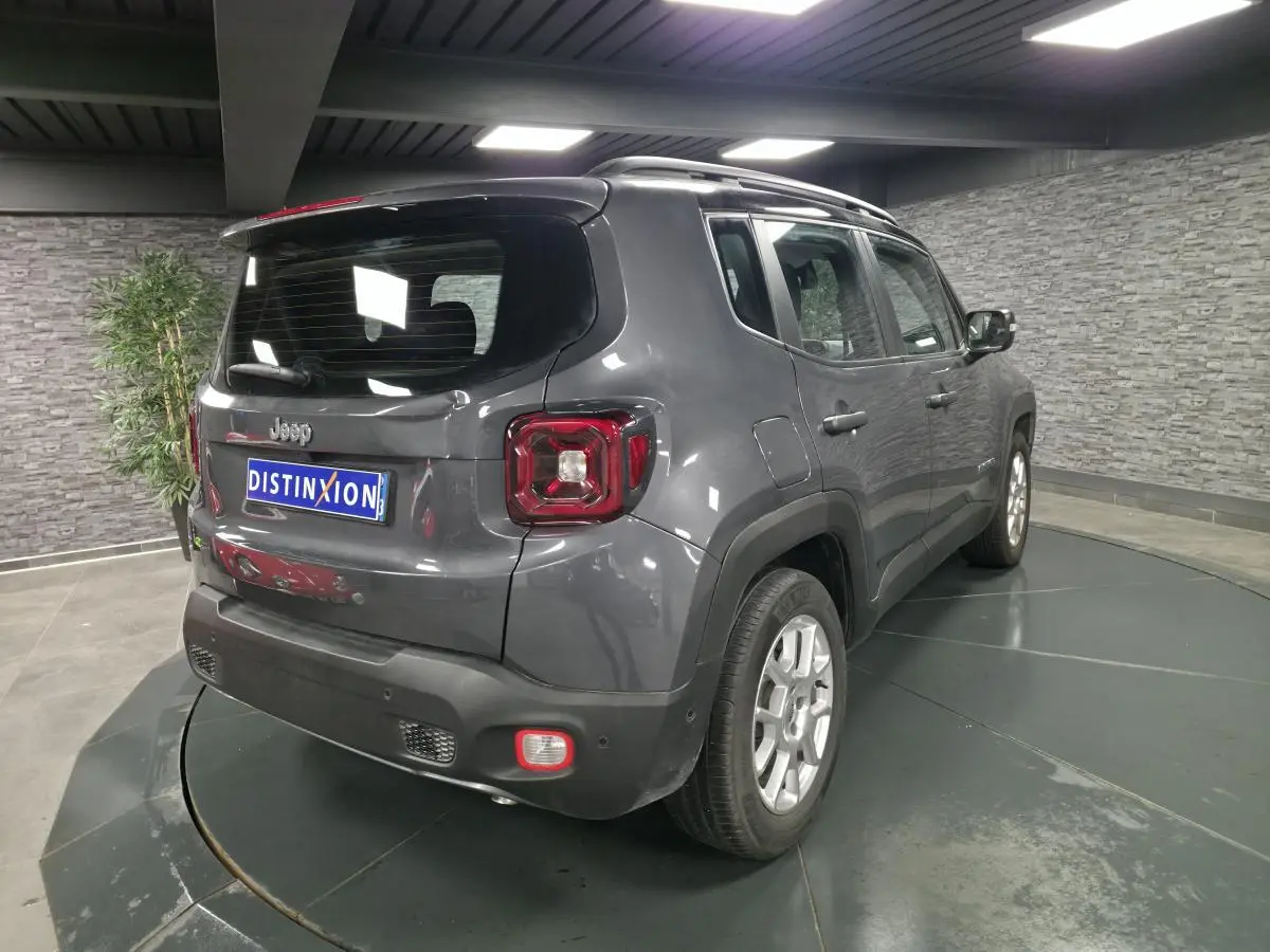 Jeep Renegade gris métallisé vu en 3/4 arrière droit dans un showroom avec toit noir et barres de toit.