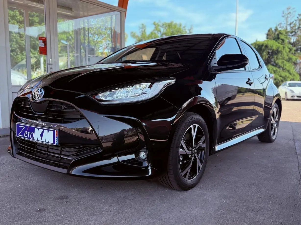 Toyota Yaris Hybrid noire vue en 3/4 avant droit, avec jantes alliage et calandre imposante brillante.