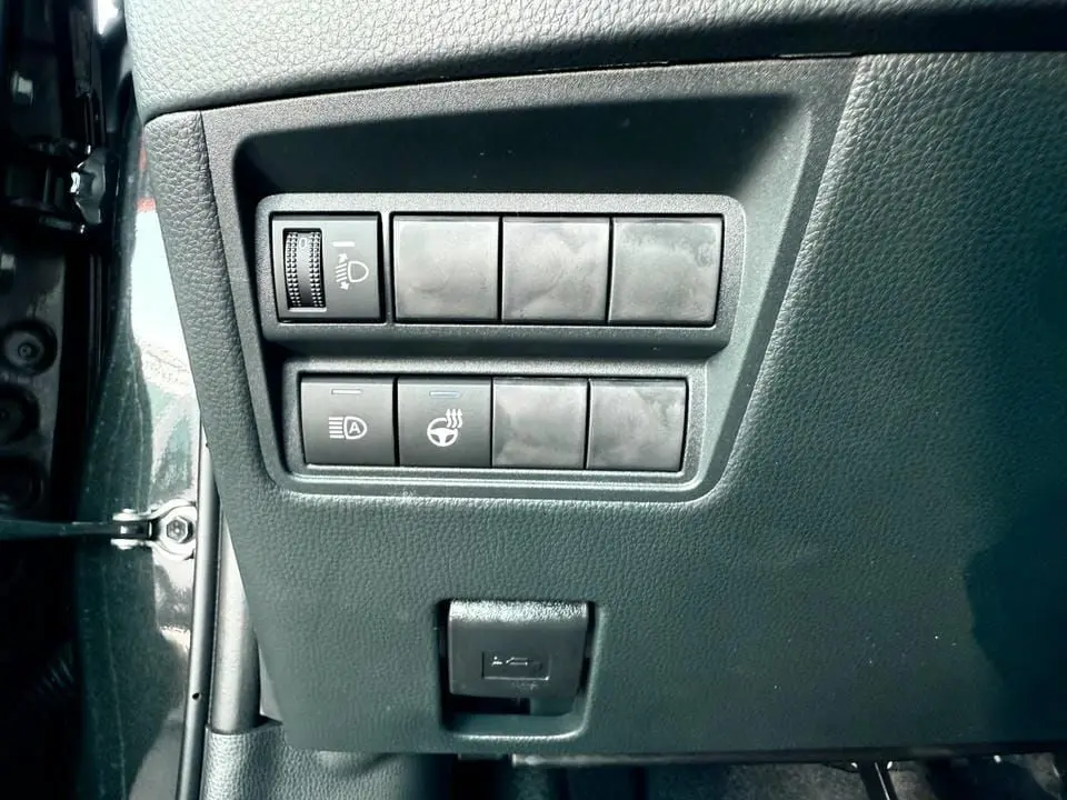Gros plan sur les commandes de réglage des phares et du volant chauffant dans une Toyota Yaris Hybrid 2025 noire.