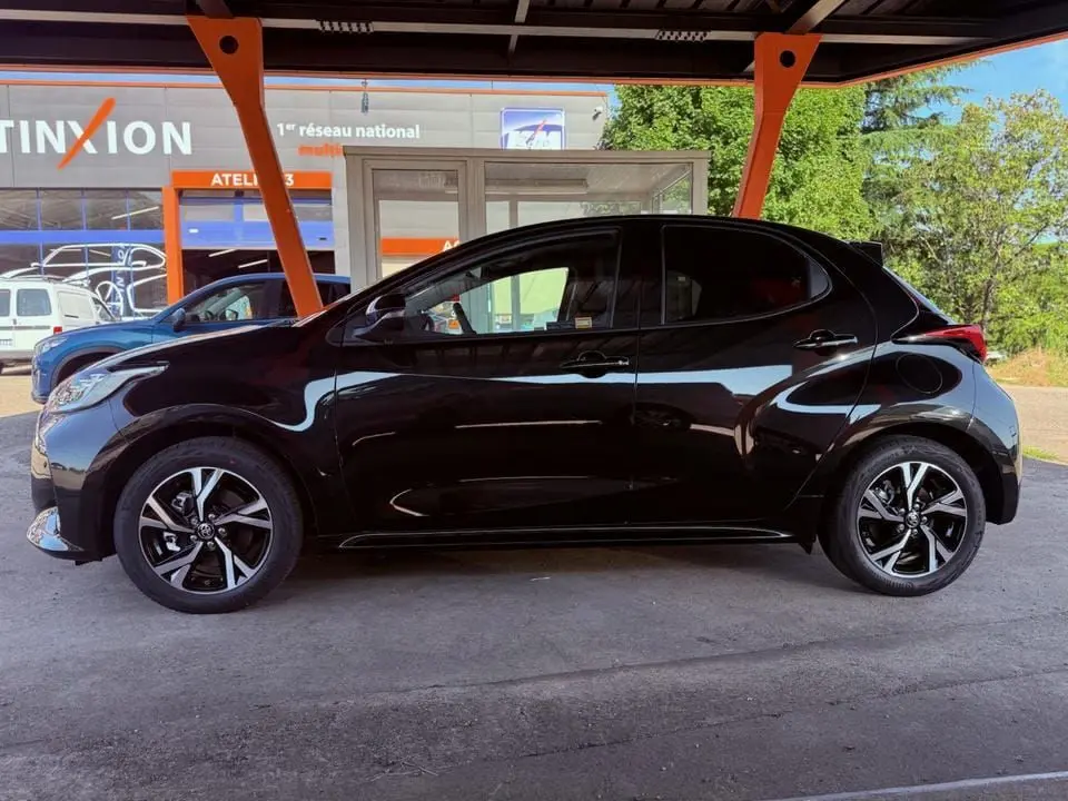 Profil côté gauche d'une Toyota Yaris Hybrid noire 2025, soulignant ses jantes alliage et lignes compactes sous un abri.