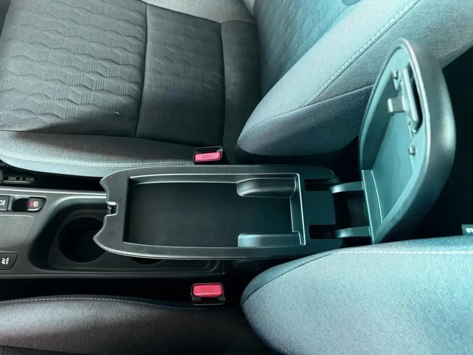 Vue rapprochée de la console centrale ouverte entre les sièges avant gris foncé d'une Toyota Yaris hybride 2025.