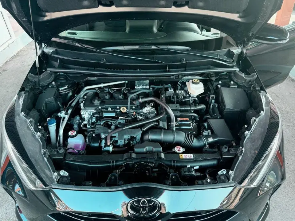Vue plongeante sur le moteur d'une Toyota Yaris noire avec capot ouvert, montrant les composants du compartiment moteur.