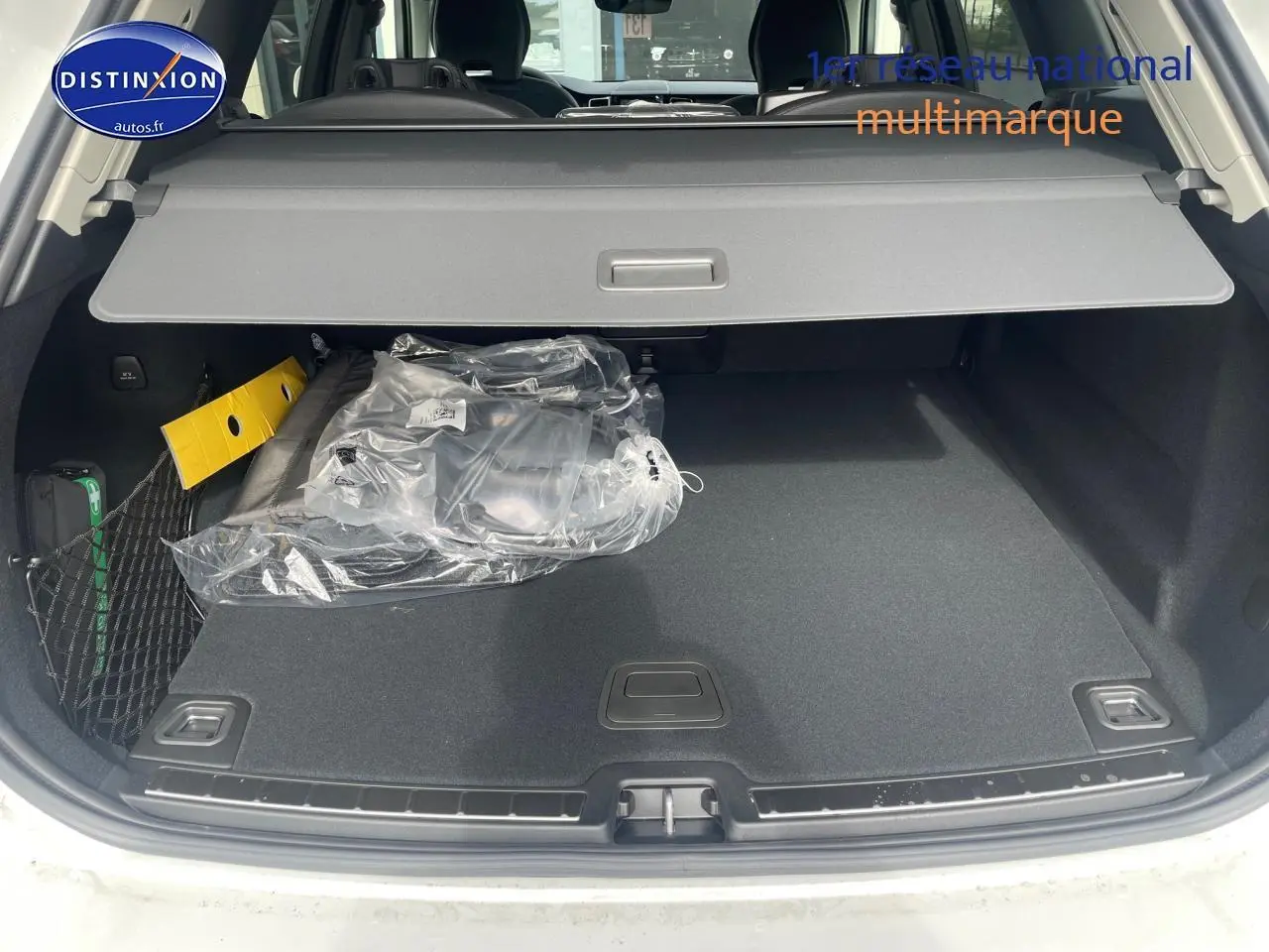Coffre ouvert d'un Volvo XC60 gris 2024, montrant la tablette cache-bagages et un filet de rangement latéral.