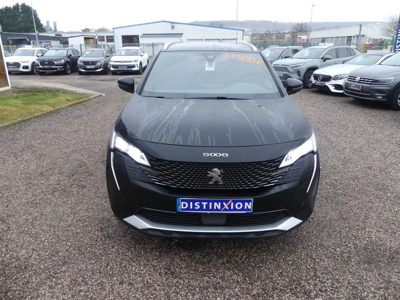 Vue frontale d'un Peugeot 5008 GT noir métallisé avec calandre chromée et feux LED allumés sur un parking.