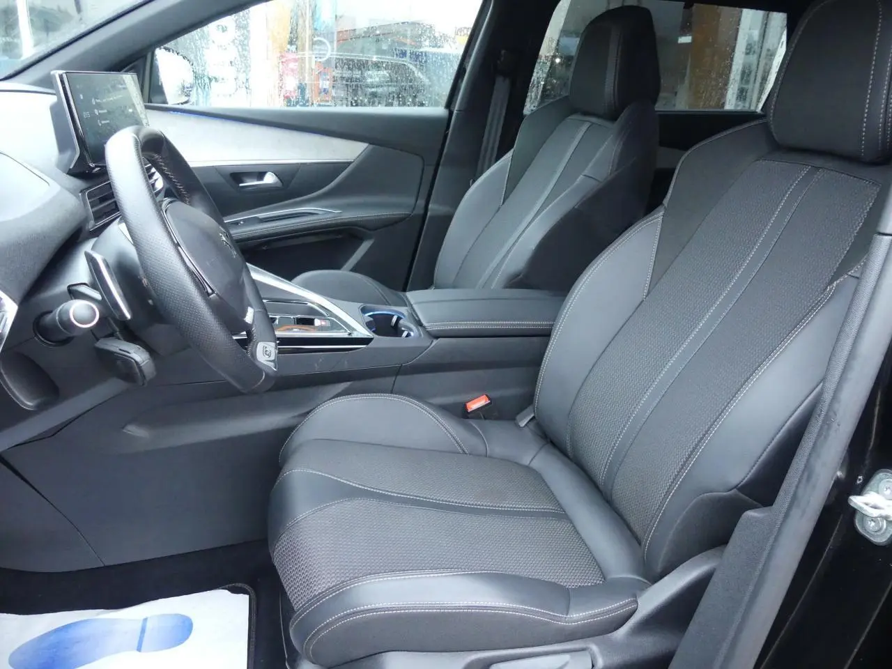 Vue intérieure côté conducteur du Peugeot 5008 GT 2023, sièges avant noirs en cuir et tissu avec surpiqûres contrastées.