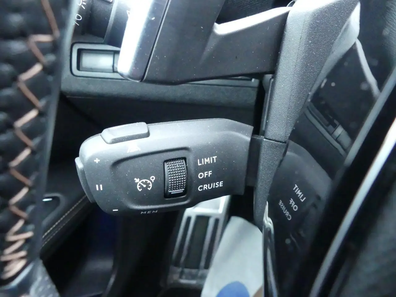 Gros plan sur la commande de régulateur de vitesse noire à gauche du volant cuir perforé du Peugeot 5008 GT noir métallisé 2023.