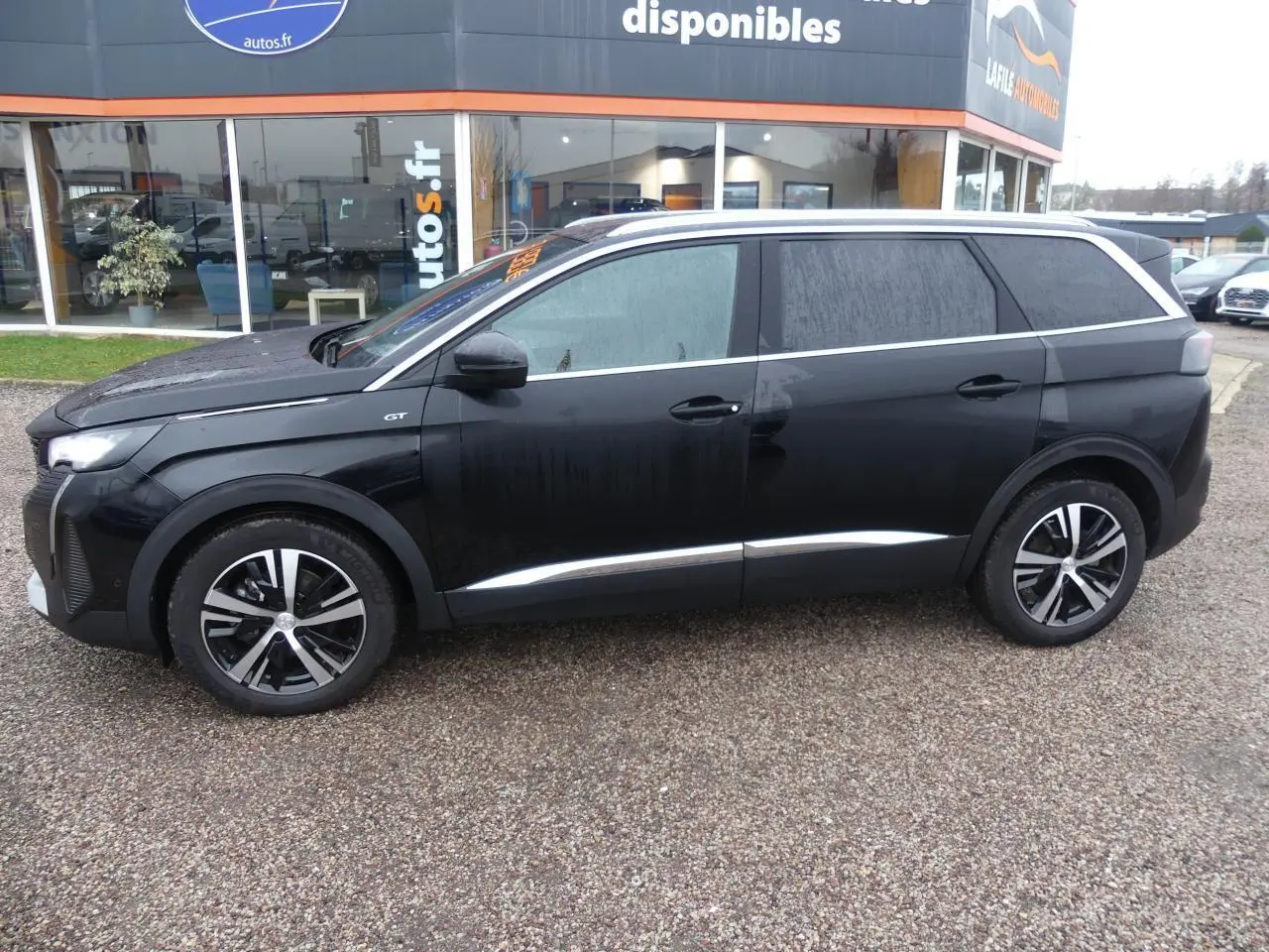 Profil droit d'un Peugeot 5008 GT 2023 noir métallisé avec jantes bi-ton et barres de toit en aluminium.