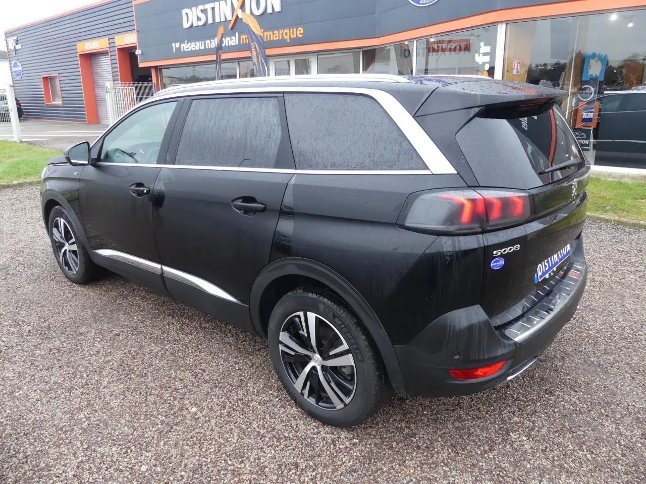 Peugeot 5008 GT noir métallisé vue 3/4 arrière droit, jantes bi-ton et barres de toit aluminium visibles.