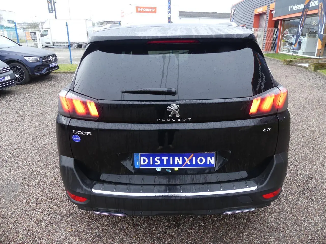 Vue arrière d'un Peugeot 5008 GT noir métallisé avec feux arrière LED allumés et double sortie d'échappement chromée.