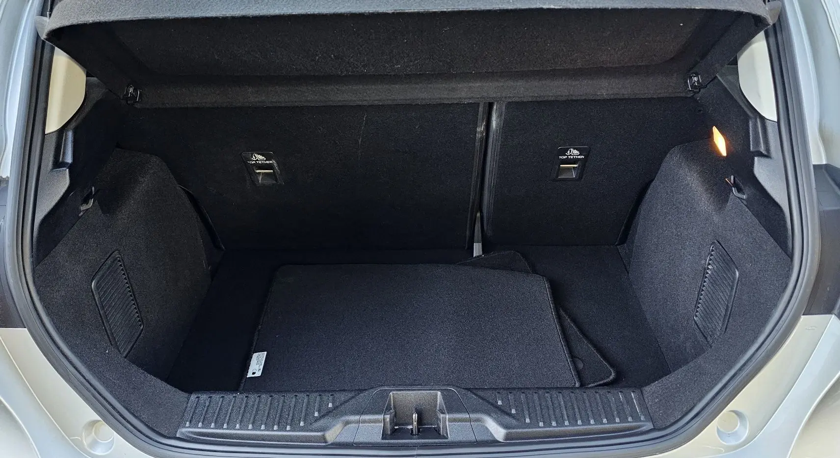 Coffre ouvert d'une Ford Fiesta gris lunaire métal 2021, montrant l'espace de rangement et les tapis noirs à l'intérieur.