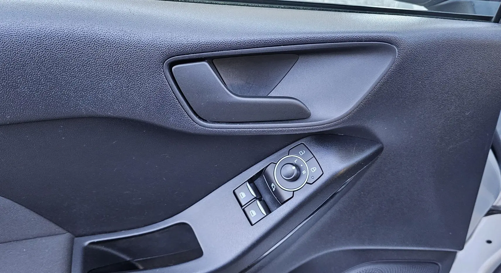 Gros plan sur la porte côté gauche d'une Ford Fiesta gris lunaire, montrant la poignée et les commandes des vitres et rétroviseurs.