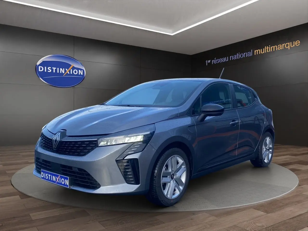 Renault Clio V E-Tech gris schiste vue 3/4 avant droit, projecteurs LED allumés en showroom.