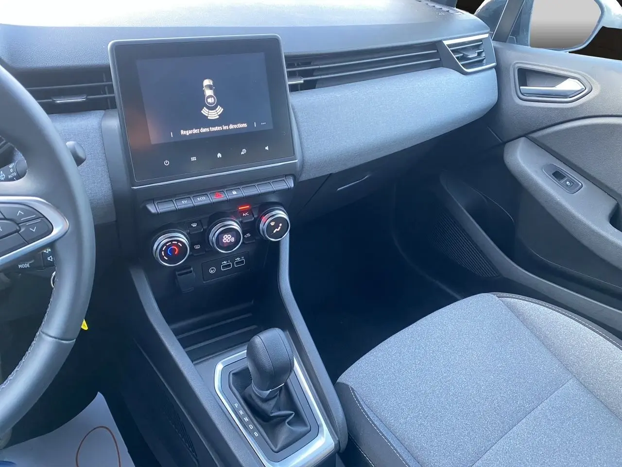 Vue intérieure côté passager de la Renault Clio V E-Tech gris schiste, avec console centrale et écran tactile visible.