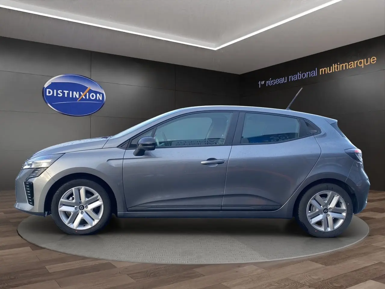 Vue de profil côté gauche d'une Renault Clio V gris schiste avec jantes alliage et antenne sur le toit dans un showroom.