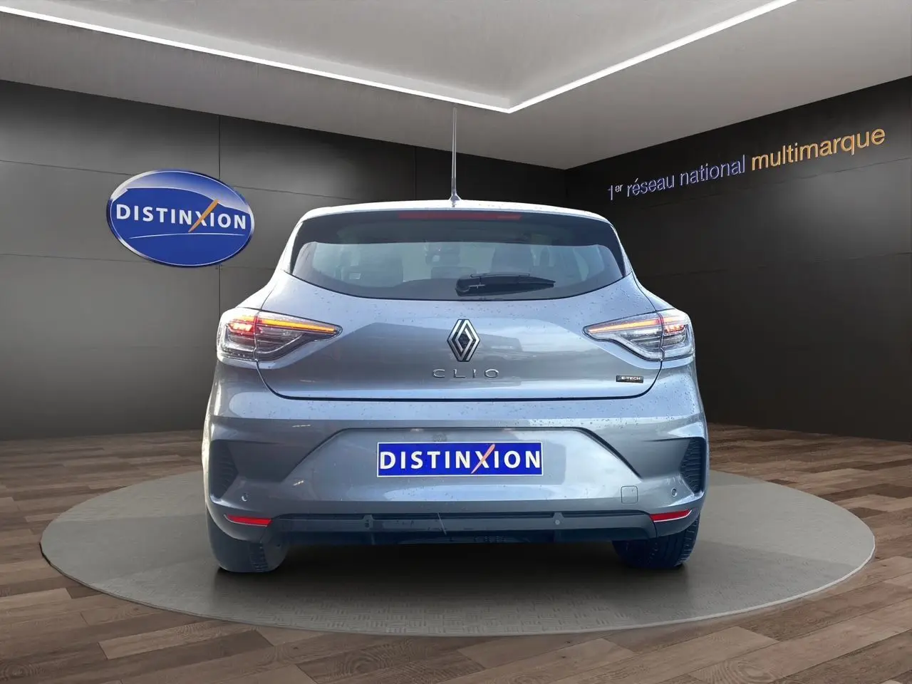 Vue arrière d'une Renault Clio V E-Tech Full Hybrid gris schiste avec feux LED allumés en intérieur showroom.