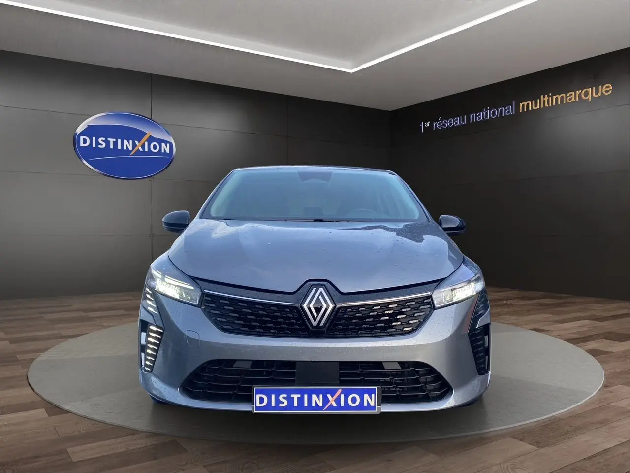 Vue avant d'une Renault Clio V E-Tech Full Hybrid gris schiste avec projecteurs LED allumés en showroom.