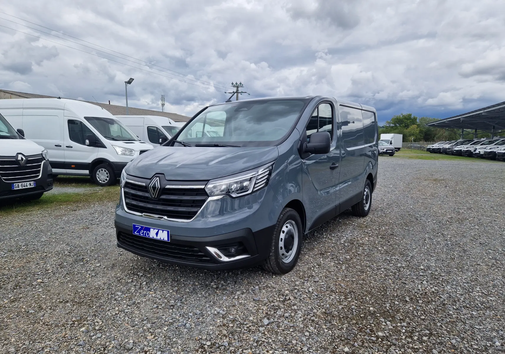 Renault Trafic Fourgon gris urbain vu en 3/4 avant droit sur un parking de véhicules utilitaires.