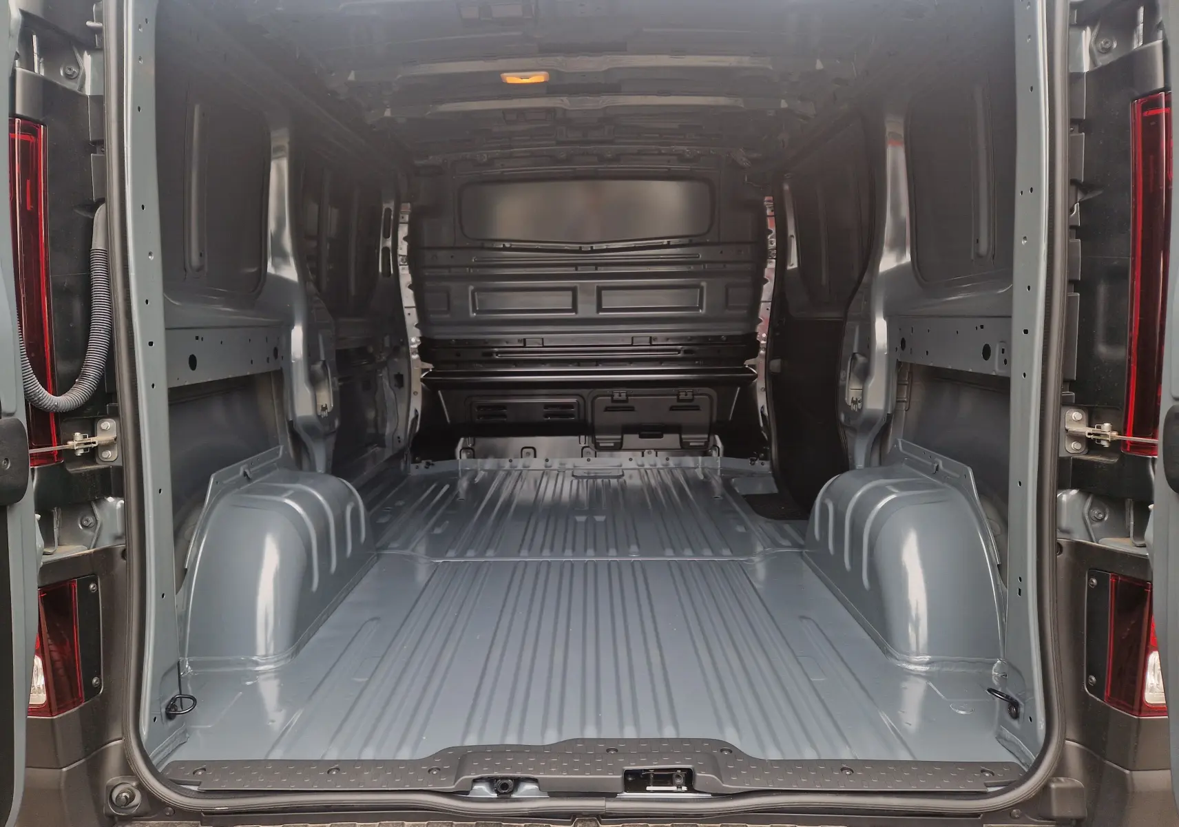 Vue intérieure arrière du Renault Trafic Fourgon gris urbain 2025, montrant l'espace de chargement vide et métallique.