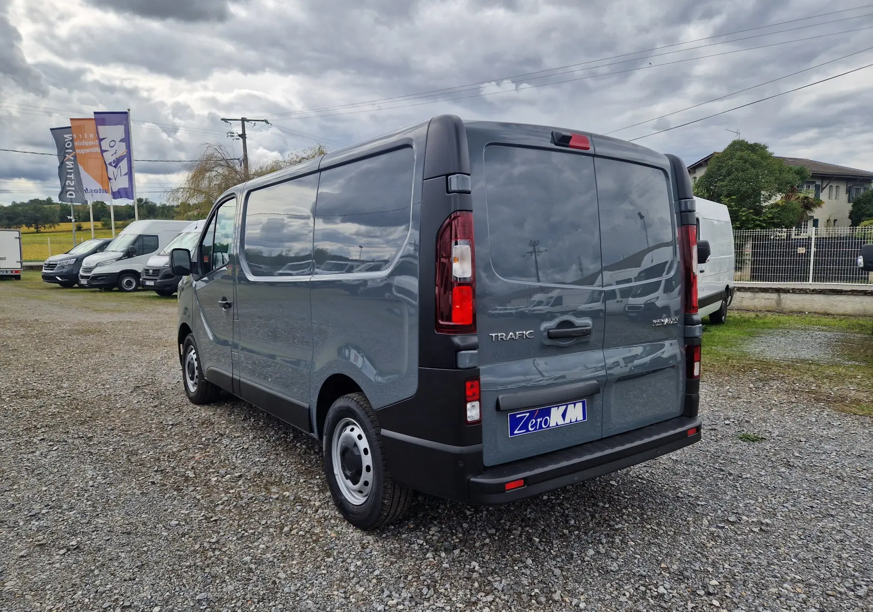Vue 3/4 arrière droite d'un Renault Trafic Fourgon gris urbain 2025 avec feux arrière verticaux et plaque Zero KM.