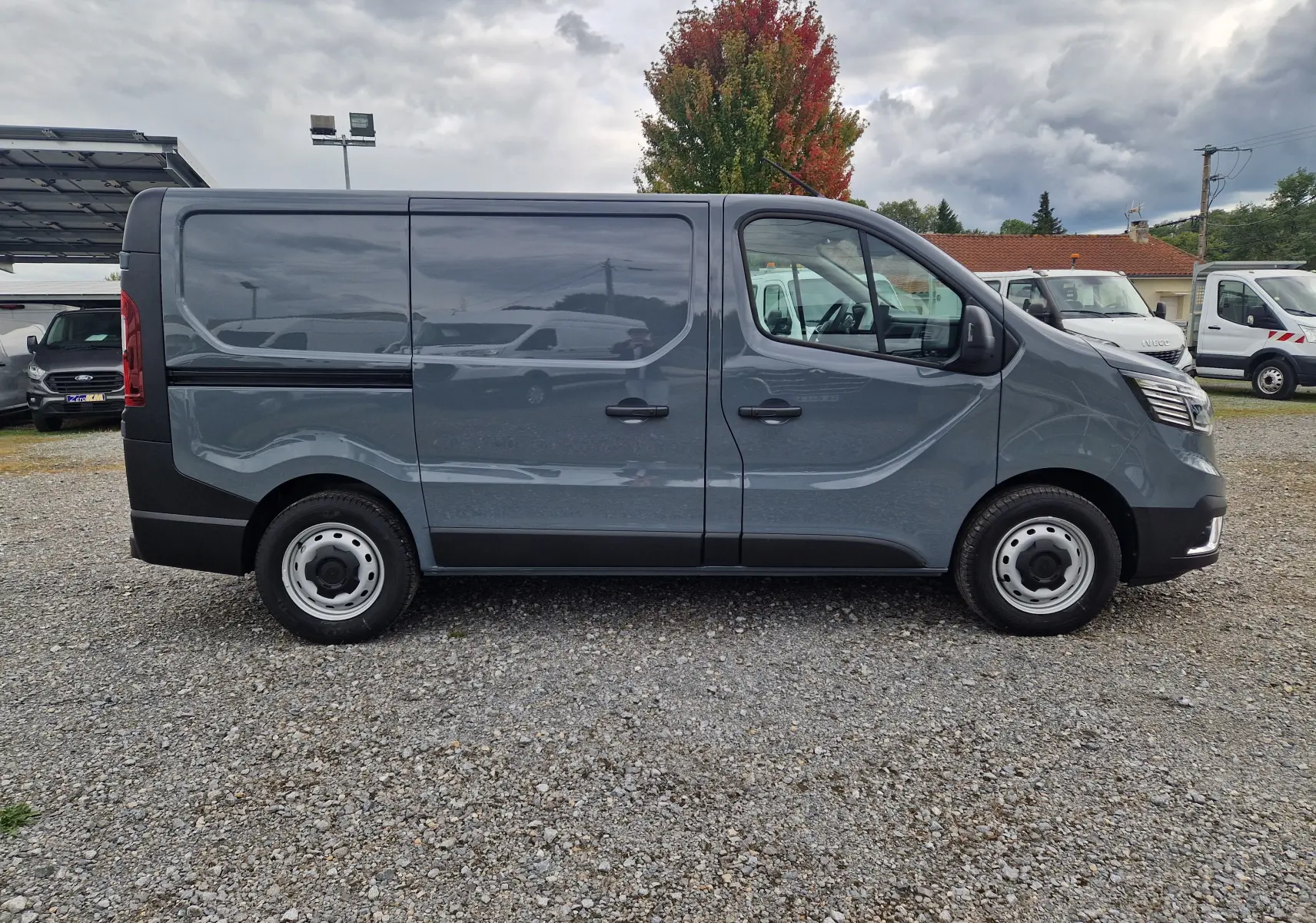 Profil droit d'un Renault Trafic Fourgon L1H1 gris urbain 2025, avec jantes acier et carrosserie lisse sans vitres latérales.