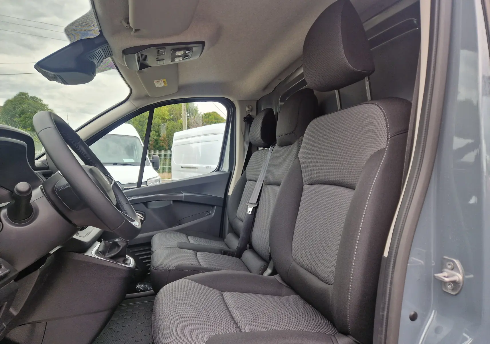 Intérieur du Renault Trafic Fourgon gris urbain 2025, vue côté droit sur les sièges avant en tissu gris et noir.