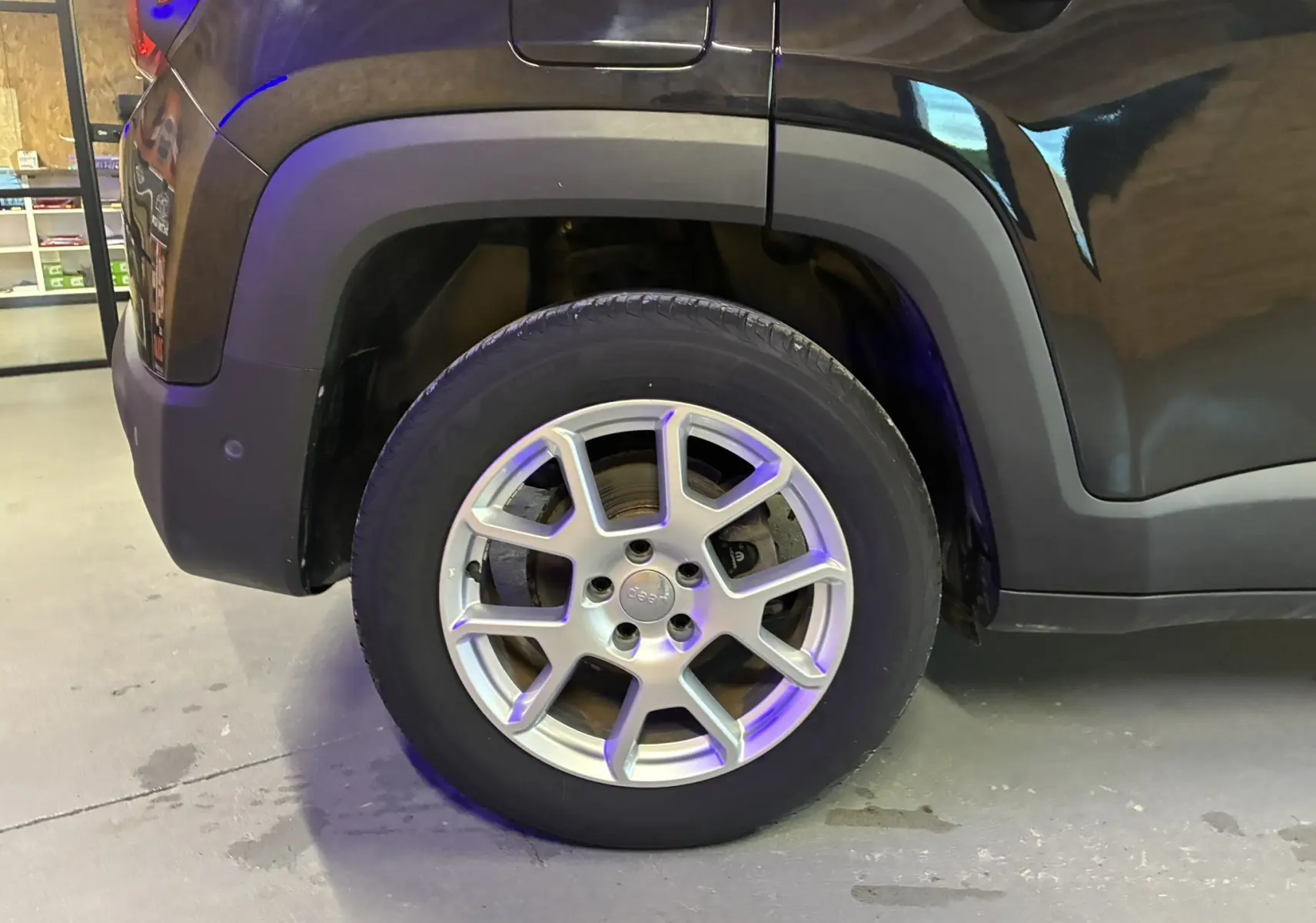 Gros plan sur la roue arrière droite d'un Jeep Renegade noir avec jante alliage argentée en intérieur.